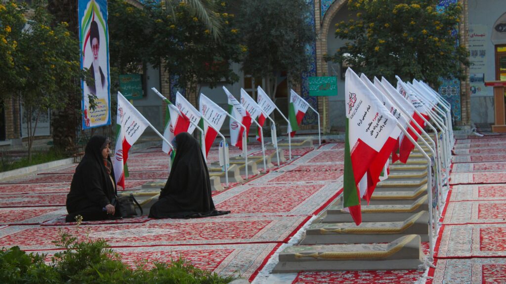 Two hijabi women sitting in a cemetery in Iran.